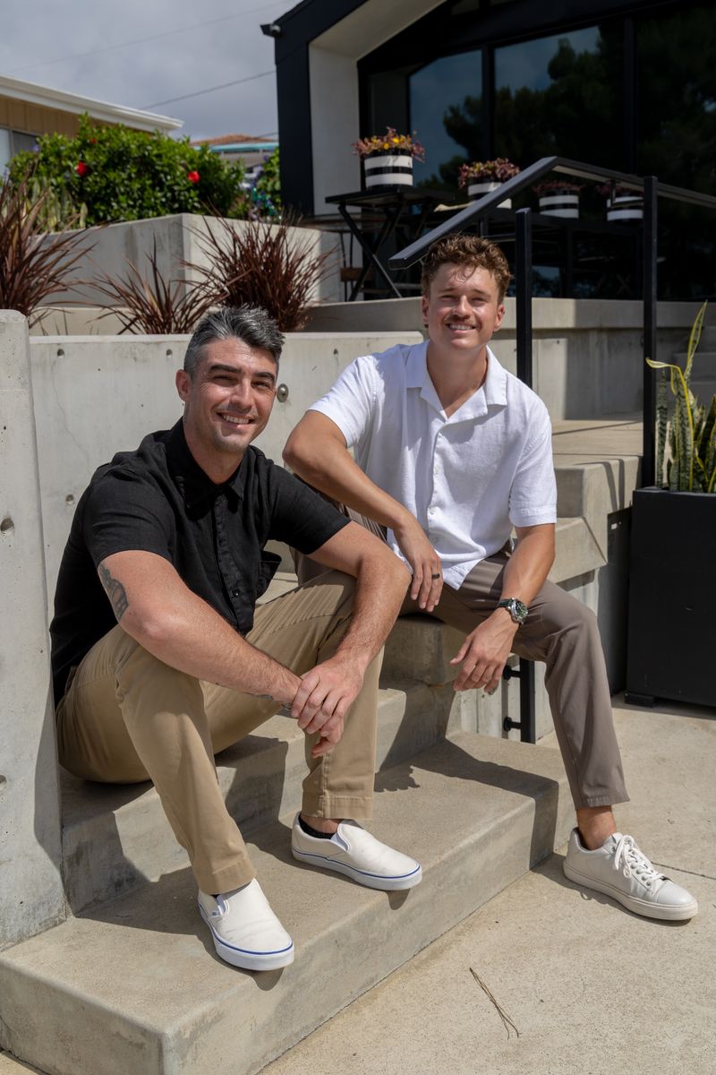 Clay and Dylan seated on concrete steps outside a modern coastal home